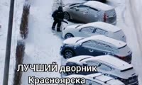 Дворник убирает снег не только с тротуара, но и сдувает его с припаркованных машин